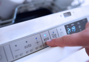 Finger som trykker på eco-knappen på oppvaskmaskin