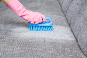 Hånd med gummihanske på renser sofa med børste.