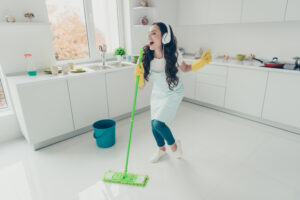 Glad jente som vasker gulv med musikk på ørene.