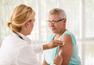 Kvinnelig helsearbeider setter vaksinespørøyten i overarmen til en kvinnelig pasient.